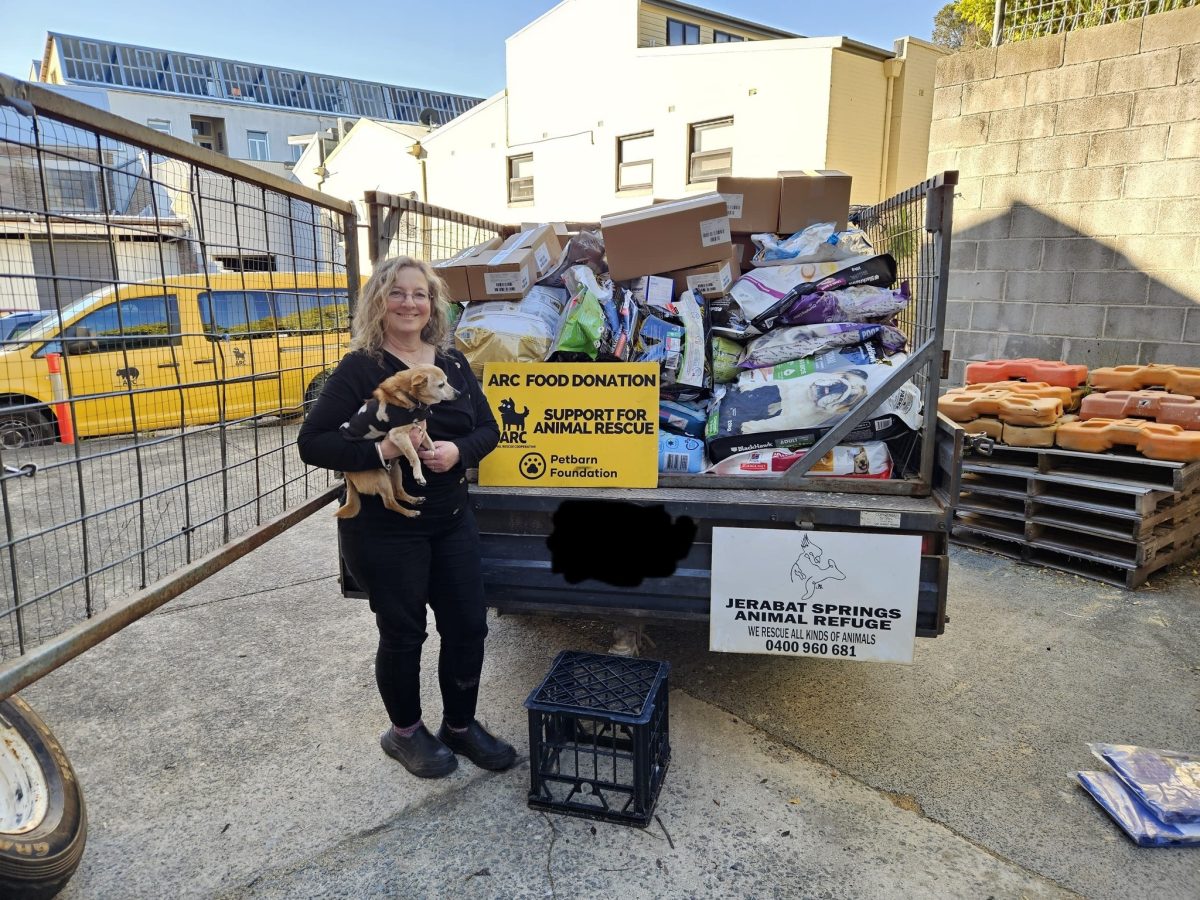 A smiling woman holding a dog next to a trailer of pet supplies
