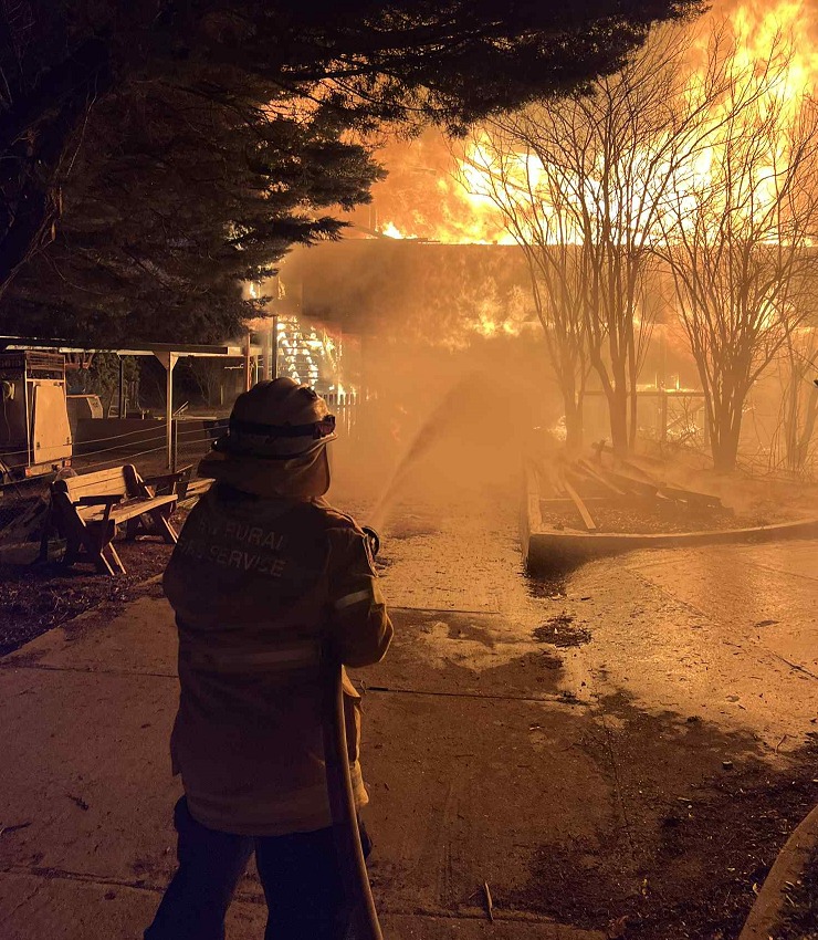 A firefighter using a hose to fight a house fire