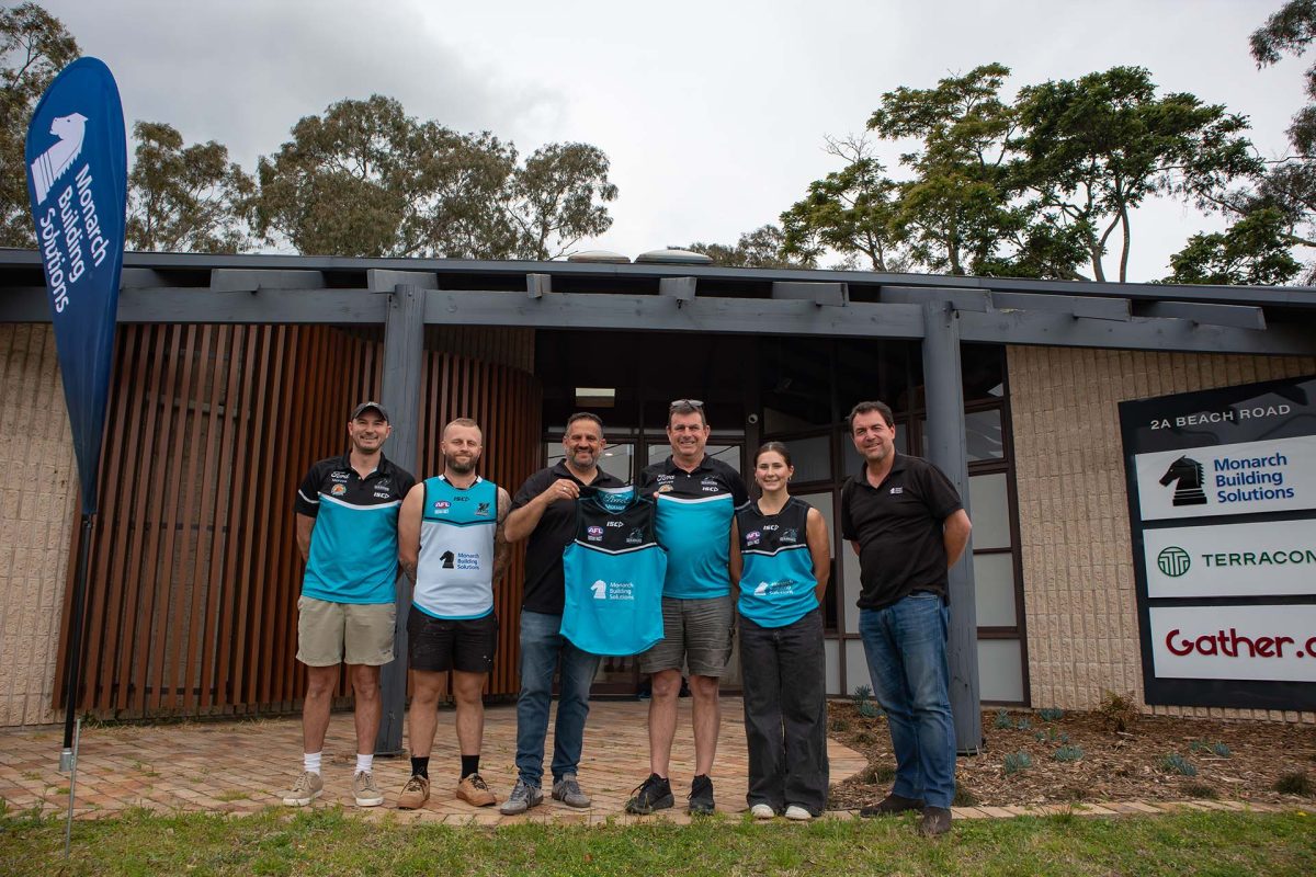 a group of people in front of Monarch Building Solutions office holding a jersey