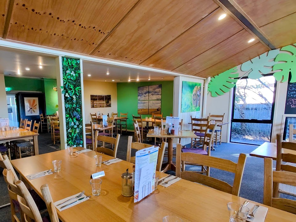 Interior shot of Cafe Woodworks, featuring a plant wall, bright green leaf cutouts on the walls, and scattered artwork featuring agricultural scenes. 