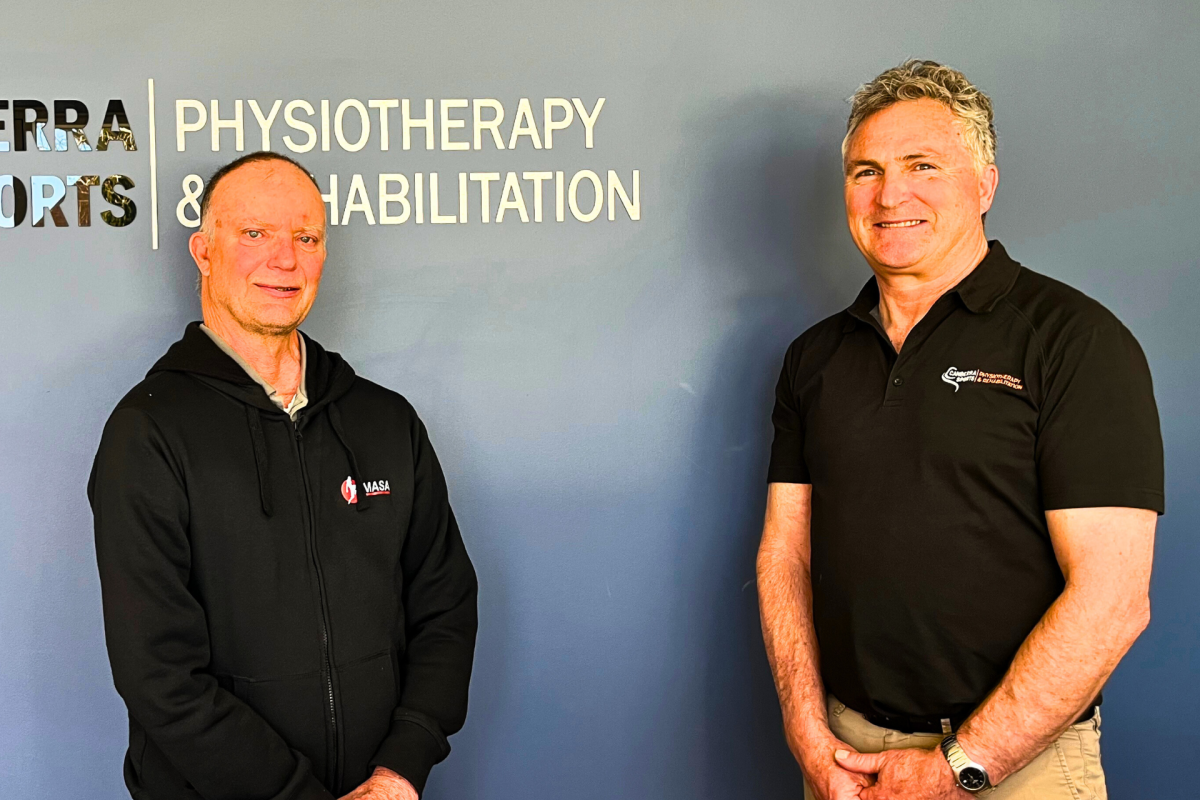 Two smiling men standing in front of a business sign