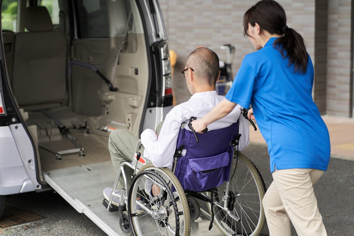 A woman pushing a man in a wheelchair up a ramp into a vehicle