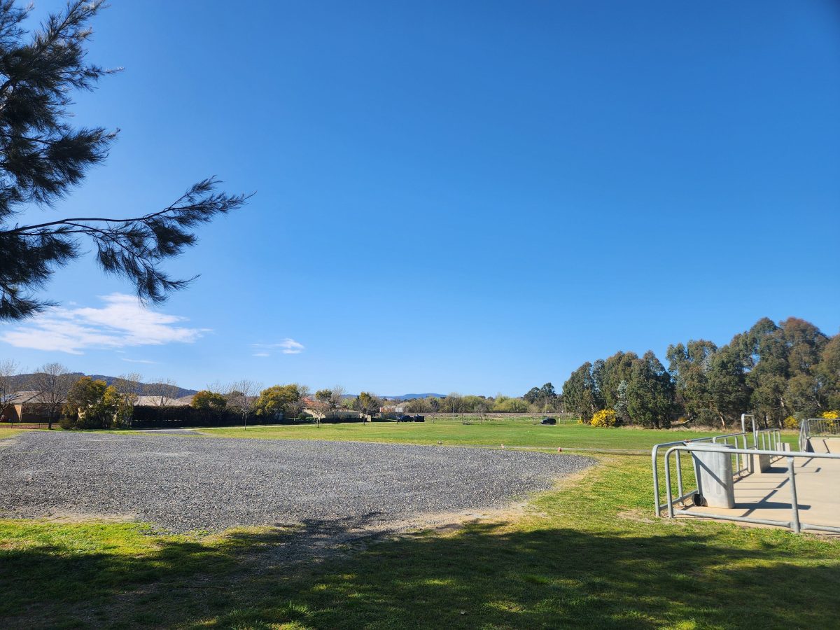 An open space with gravel and grass to the left of a skatepark