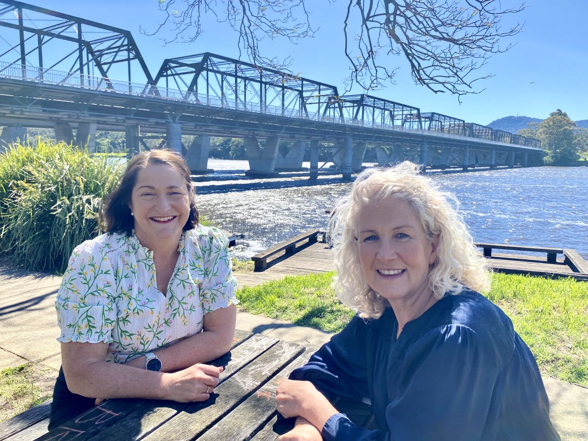 Two women sitting in front of the bridge at a park bench