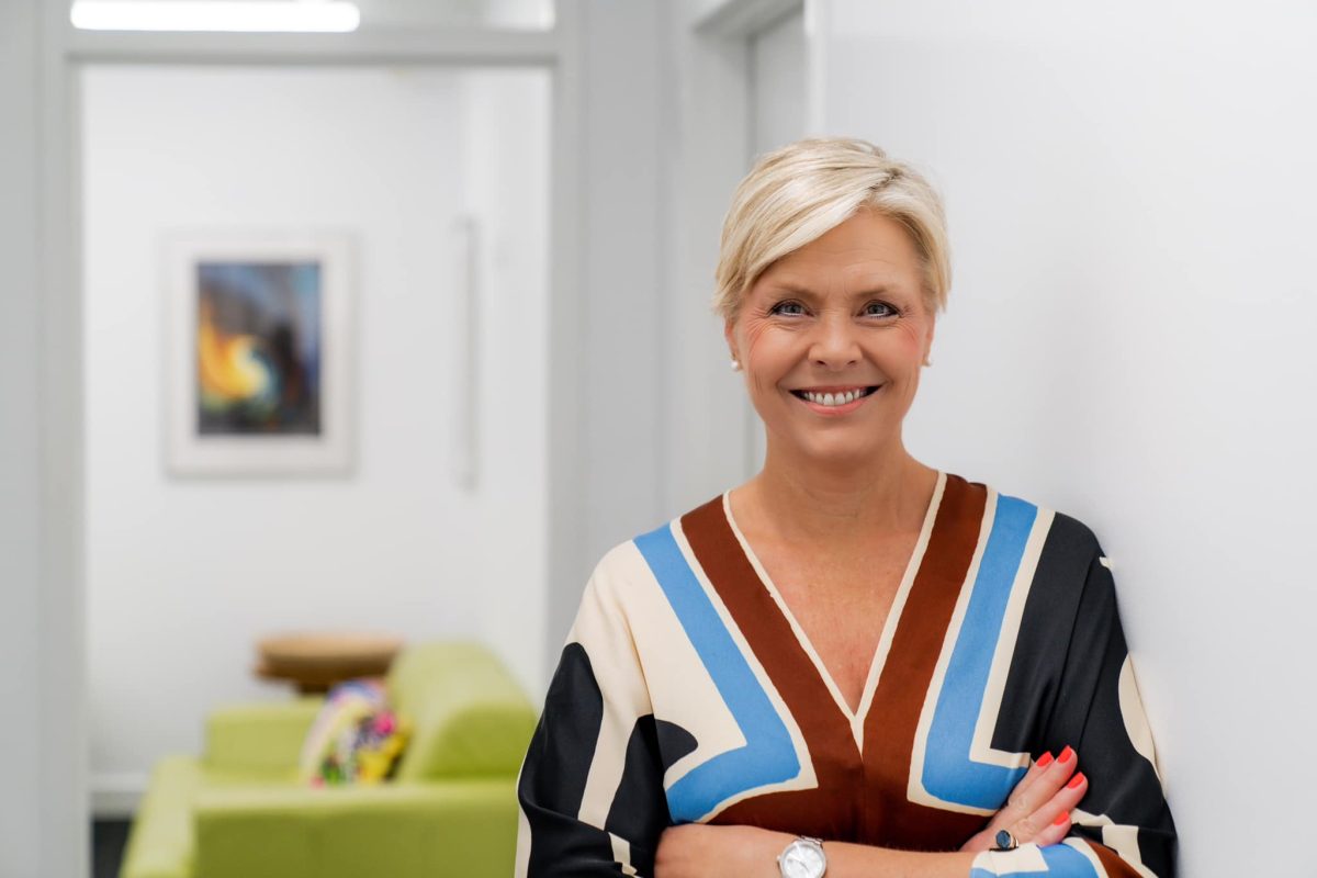A smiling woman with short blonde hair and her arms crossed