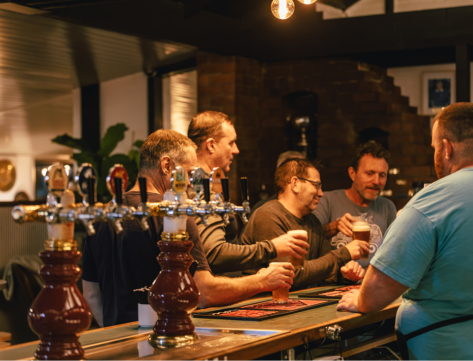 people at a bar holding schooners of beer