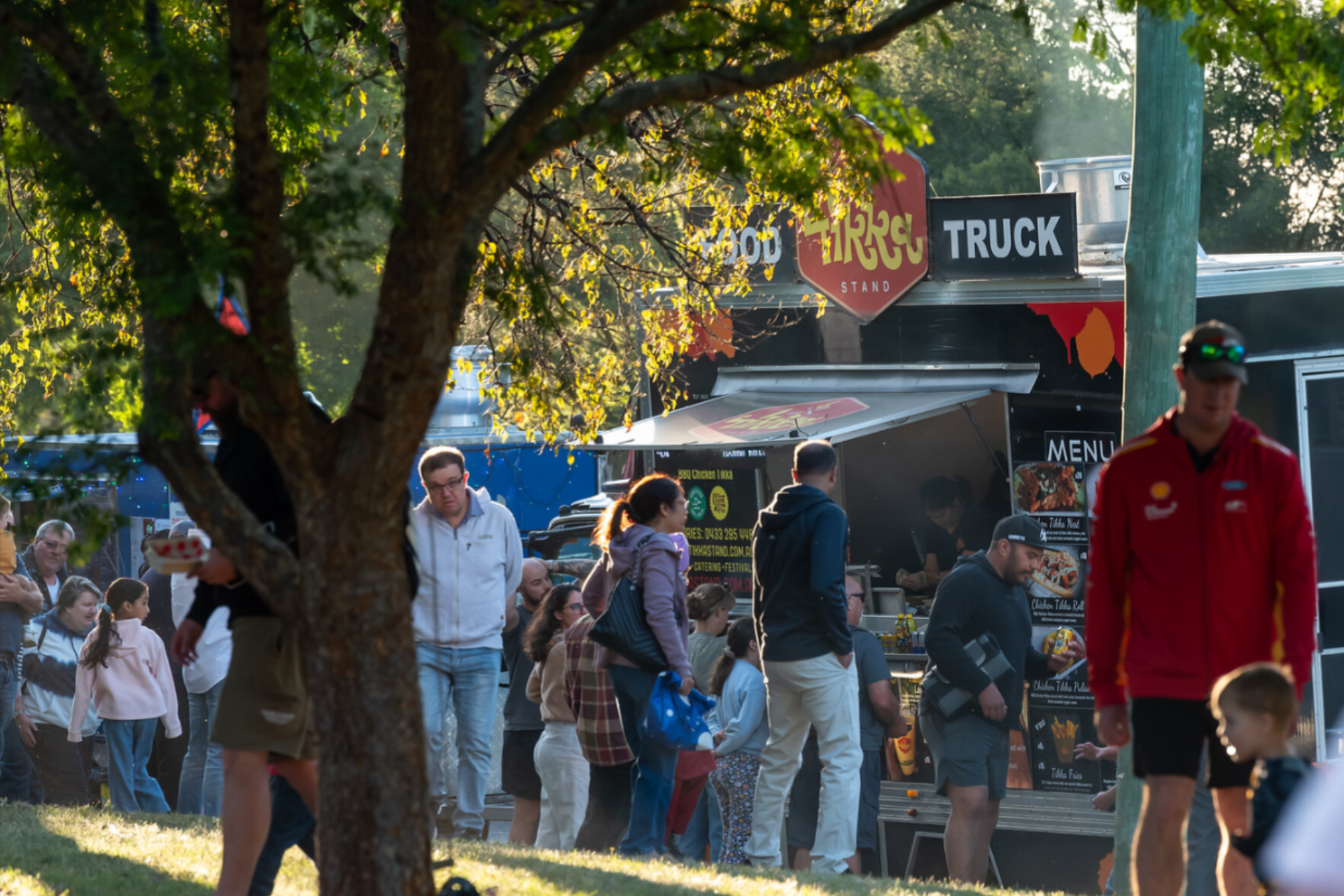 Indian food truck in a park with a crowd.