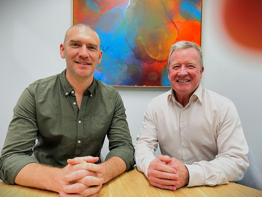 two smiling men sitting at an office desk