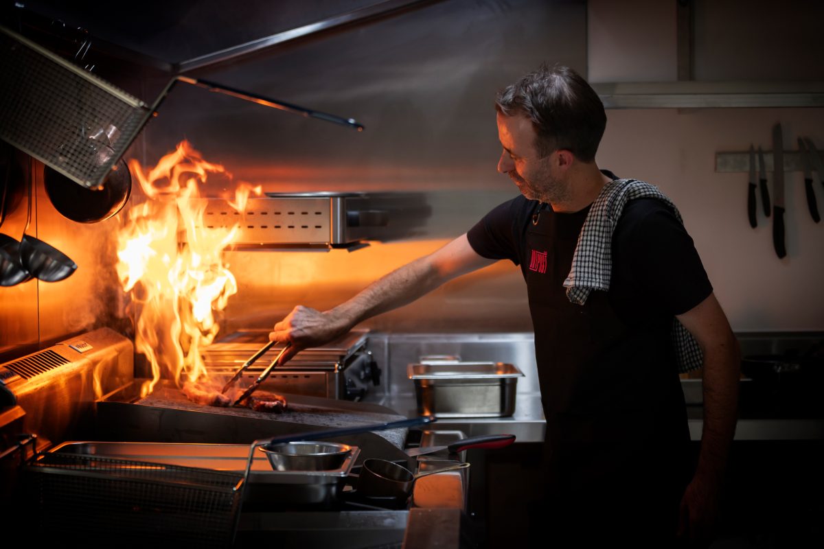 A chef with something flaming on the grill.