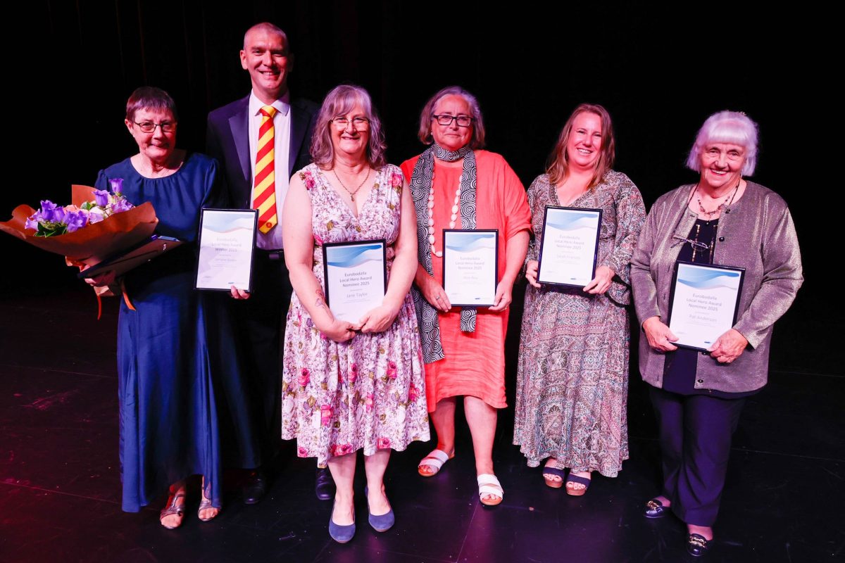 A man and five woman standing in a row, the women holding framed certificates