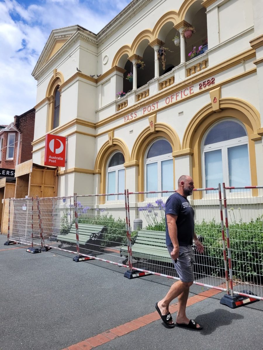 A man walking past fencing in front of Yass Post Office