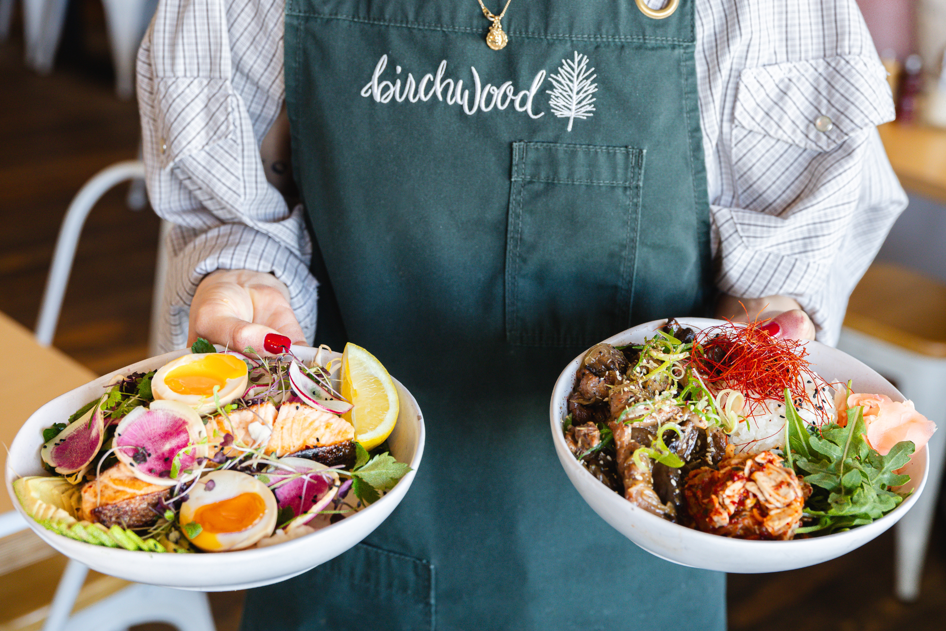 Person in an apron holds two plates of food at a cafe