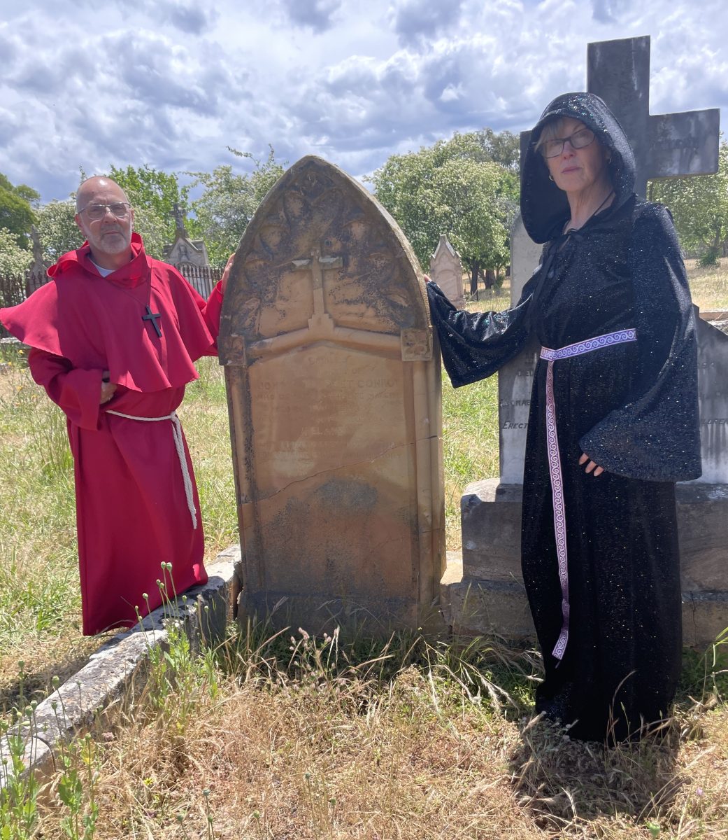 Man dressed in red habit woman in black at gravestone.