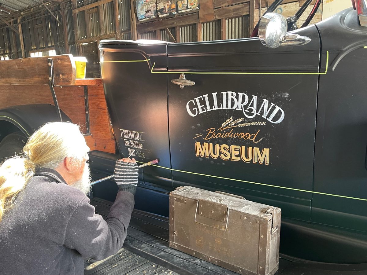 A man painting the side of a black vintage car