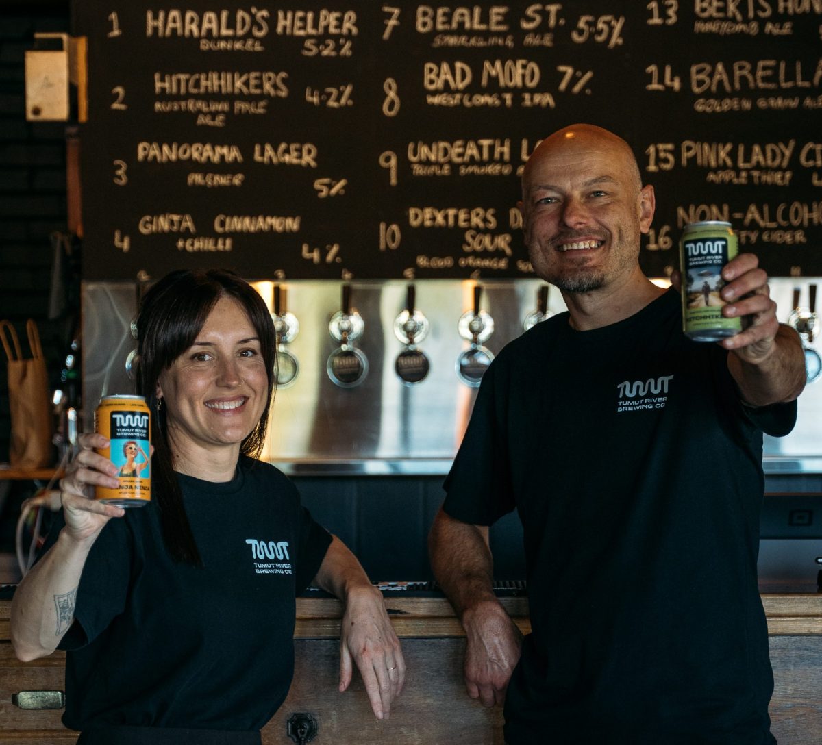 A woman and man hold beer cans up to the camera.