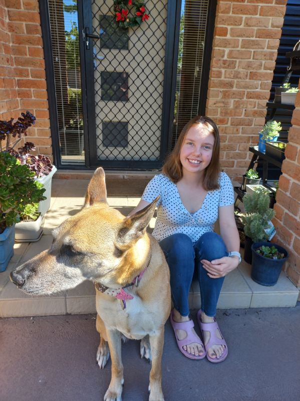 A smiling teenager with a dog, sitting on a porch stoop