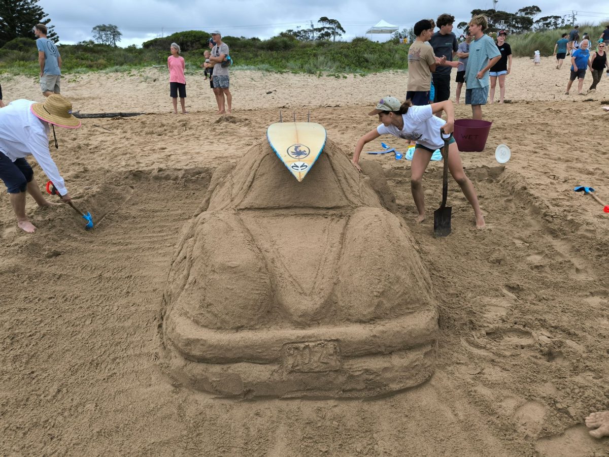 people working on car sand sculpture with surfboard on top
