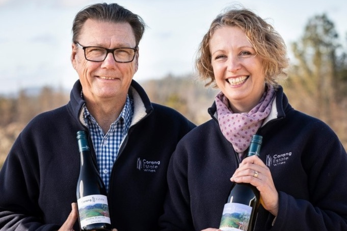 A smiling man and a smiling woman holding bottles of wine