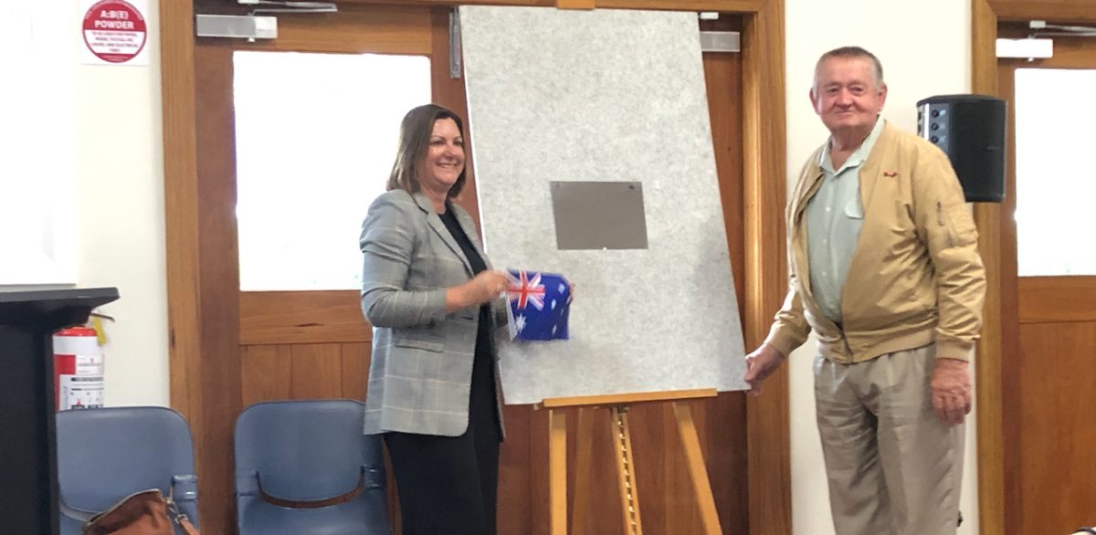 a woman and a man unveiling a plaque in a community hall