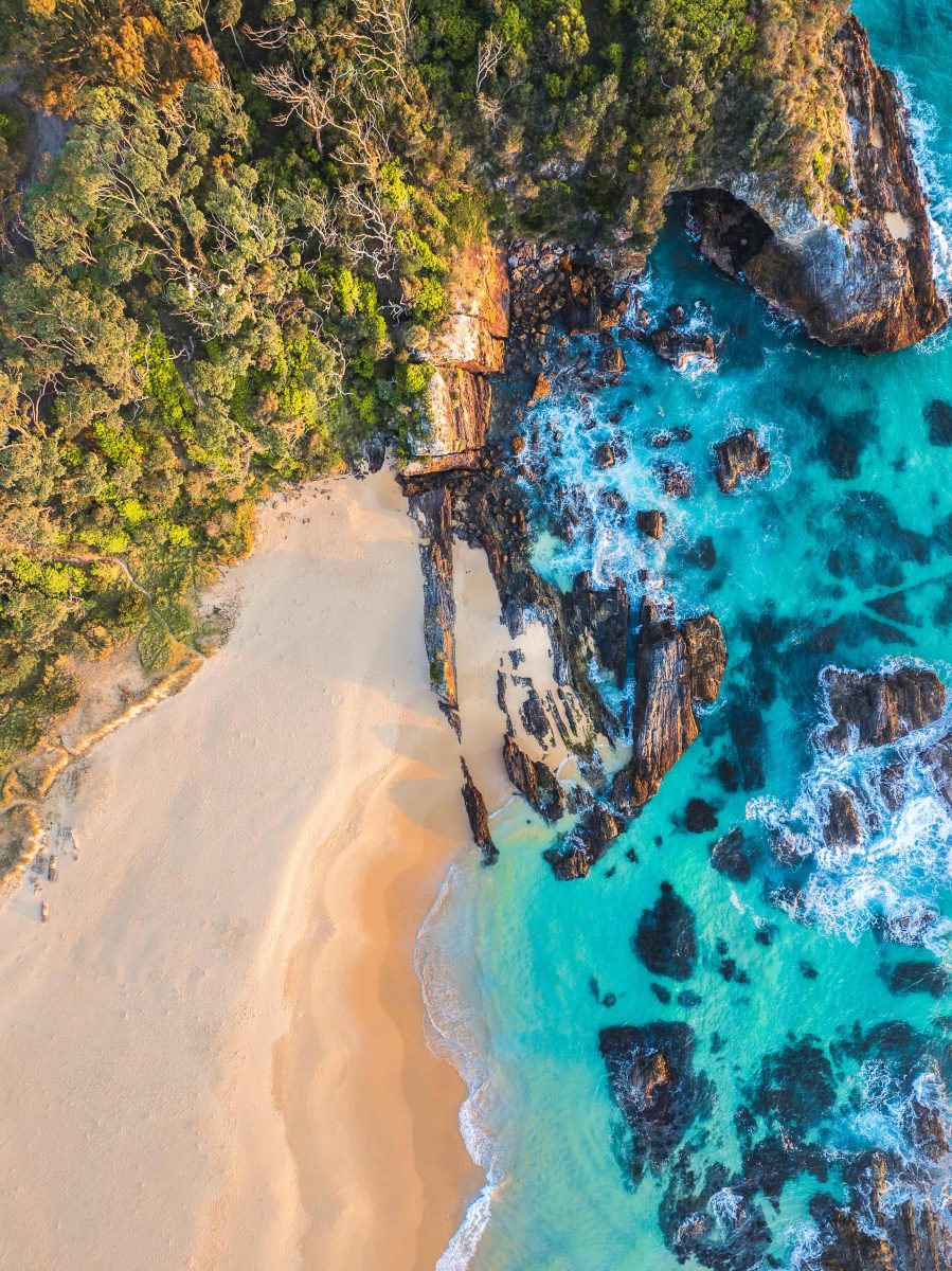 Drone shot of Mystery Bay from directly above, looking down on ragged rocks emerging from crystal clear waters.