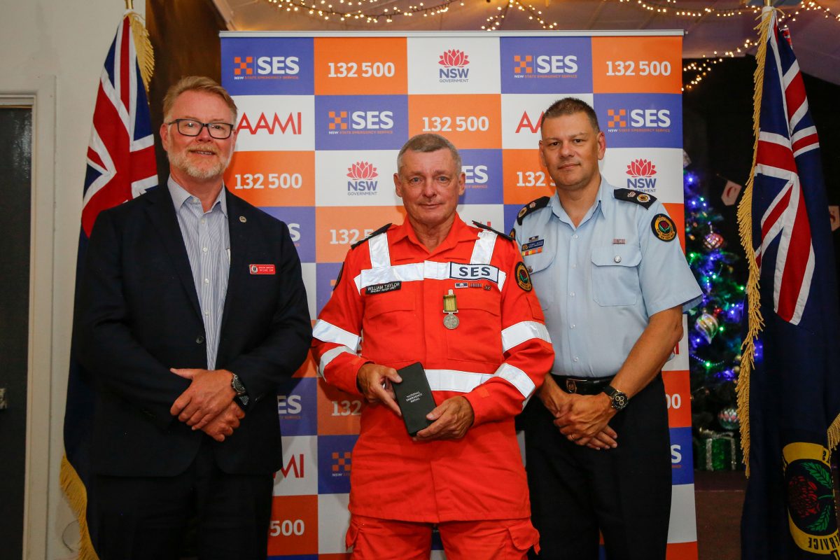 An SES worker with an award, flanked by a man in a suit and a man in a uniform