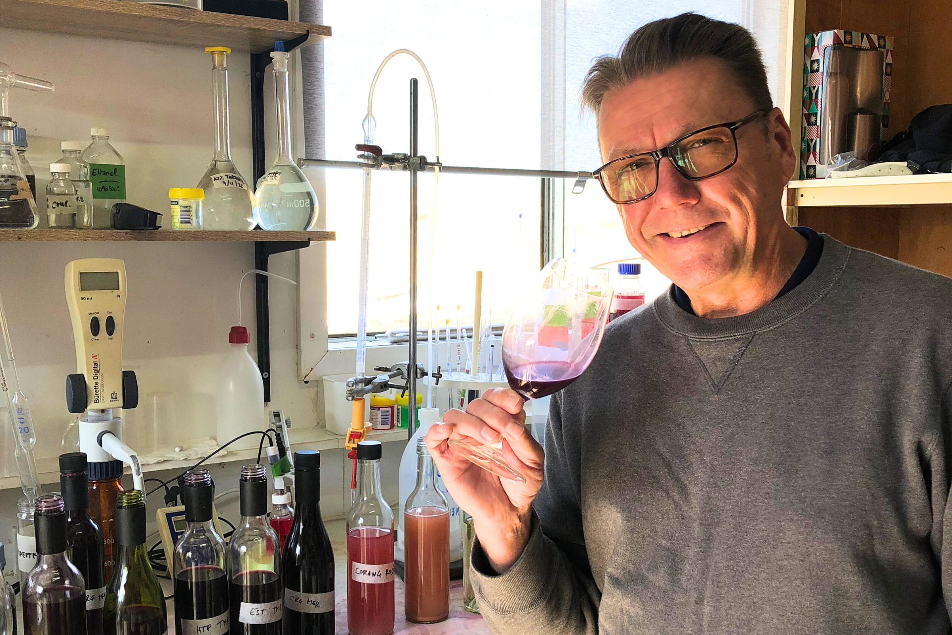 Man holding wine glass in lab-like setting.
