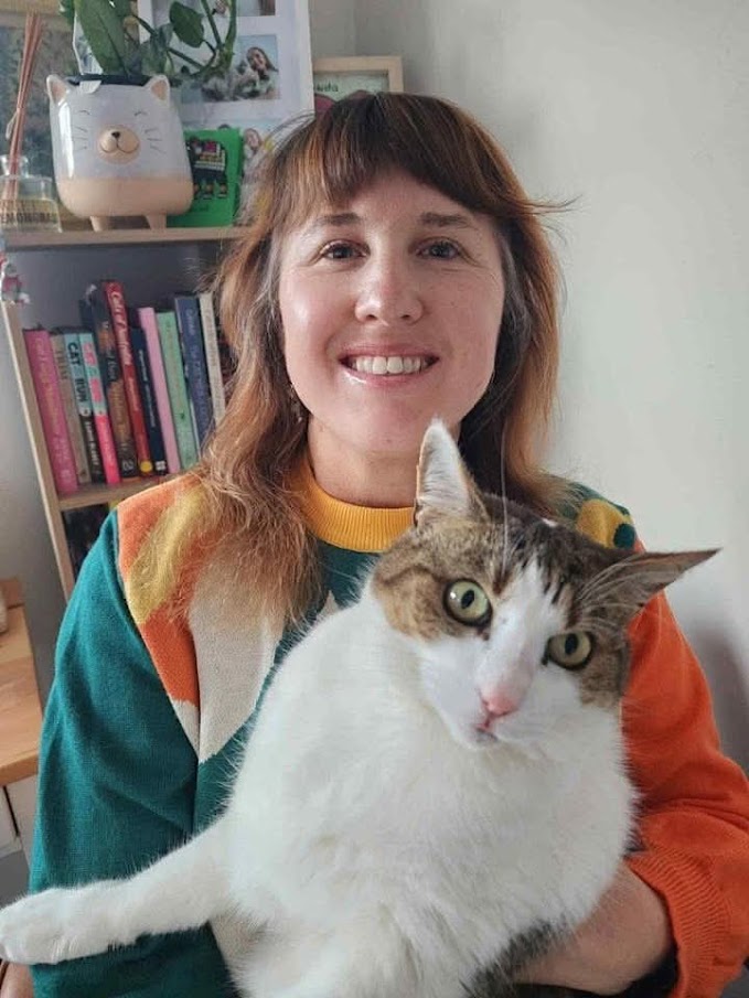 A smiling woman with brown hair holding her tabby cat