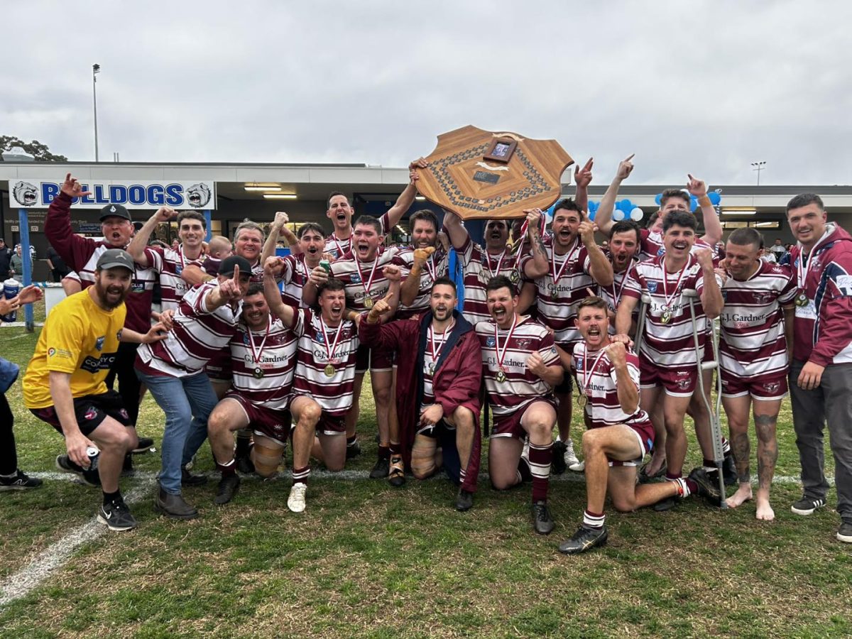 A group of players and supporters kneeling around a competition shield