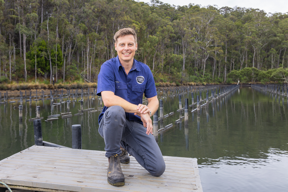 A man in branded AOC polo shirt kneels on a platform with an oyster lease behind him.