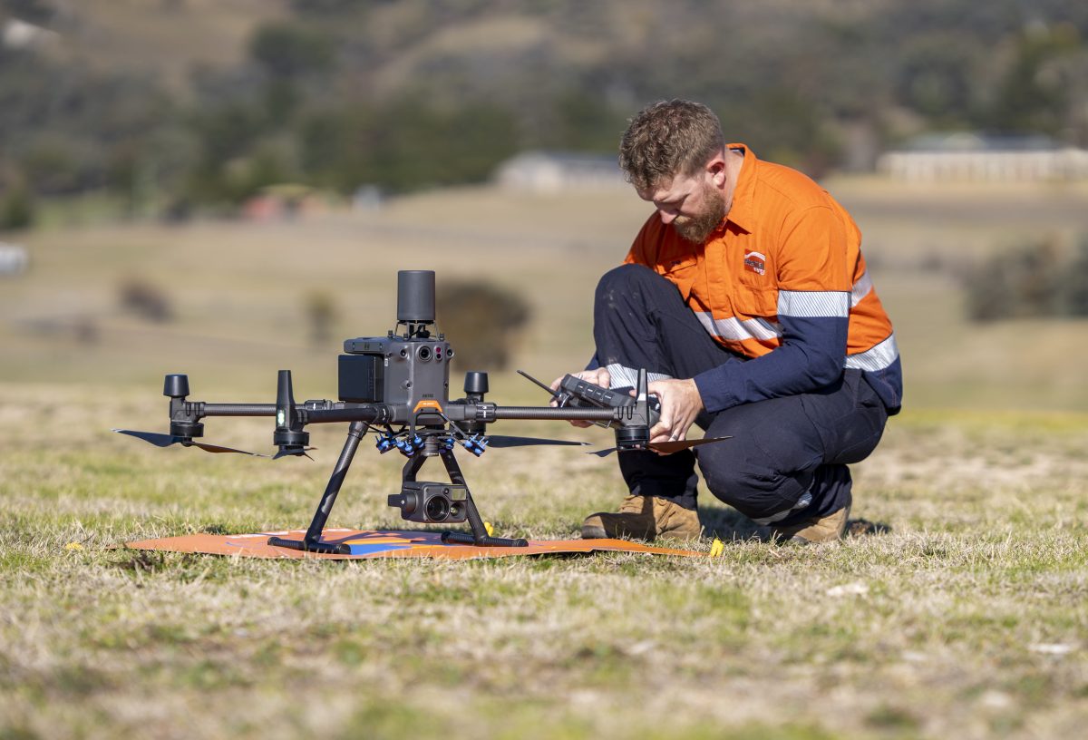 A man in orange high-vis kneeling to prepare a drone