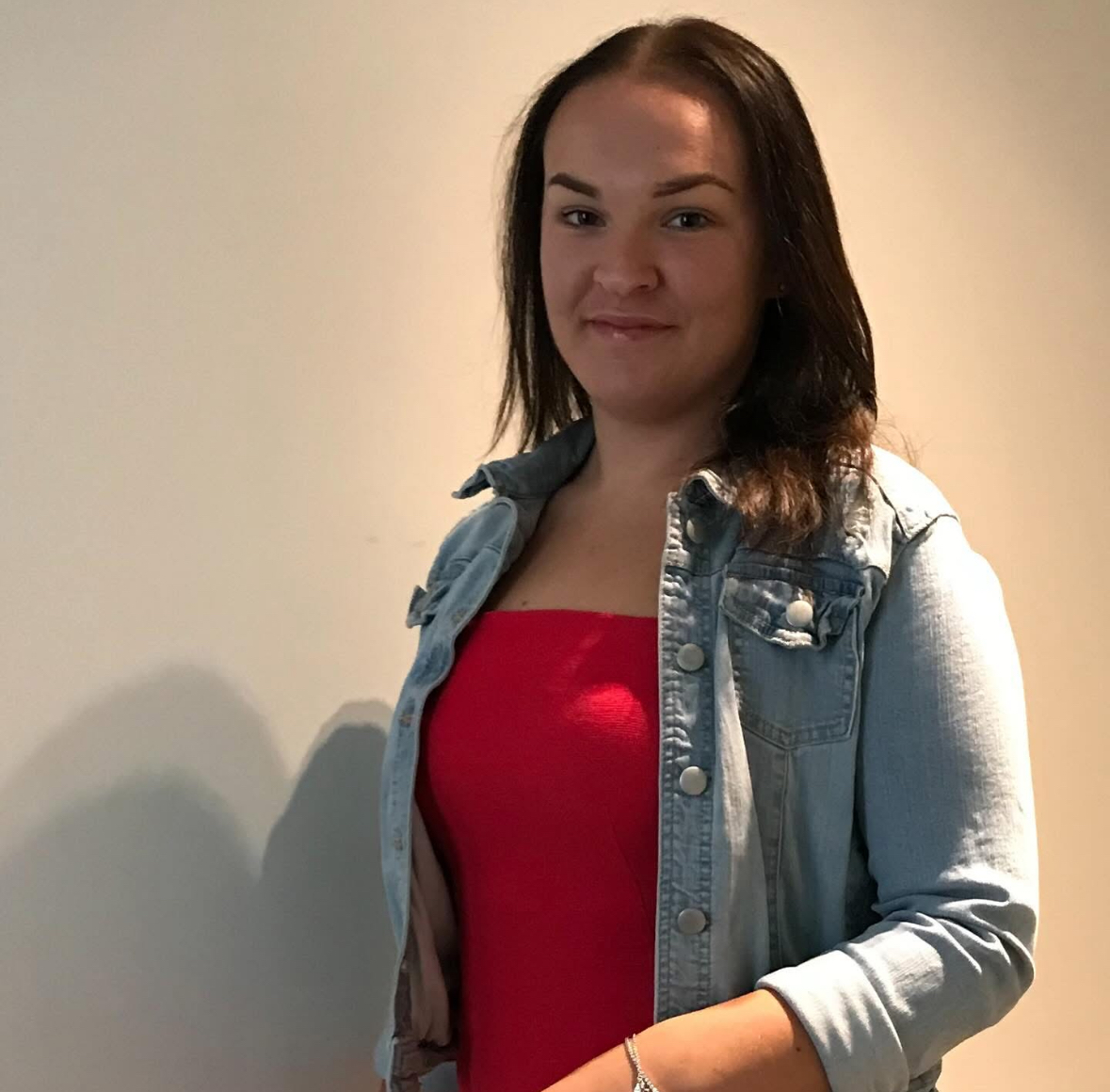 A smiling young woman with dark hair in a denim jacket
