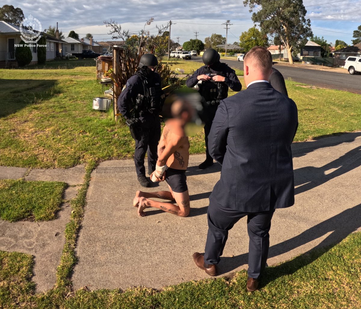 A man in handcuffs, kneeling on the ground in front of police