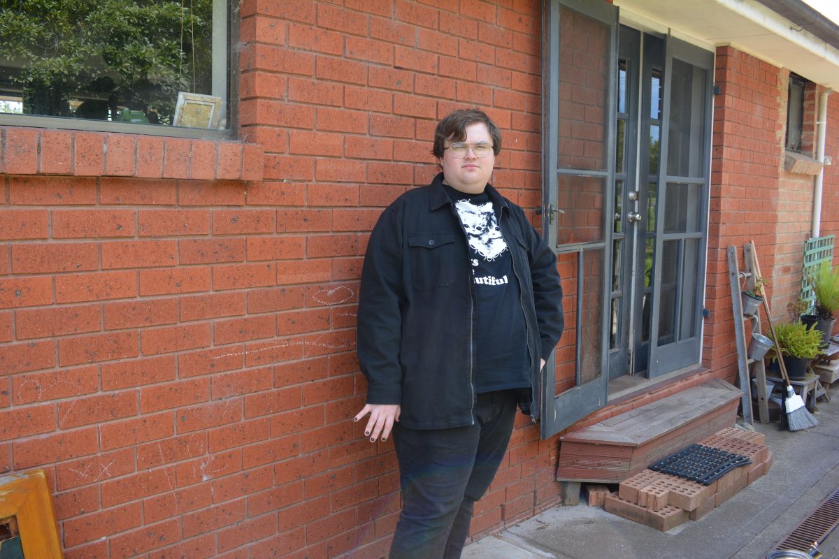 A man wearing black clothes standing against a brick wall and smiling