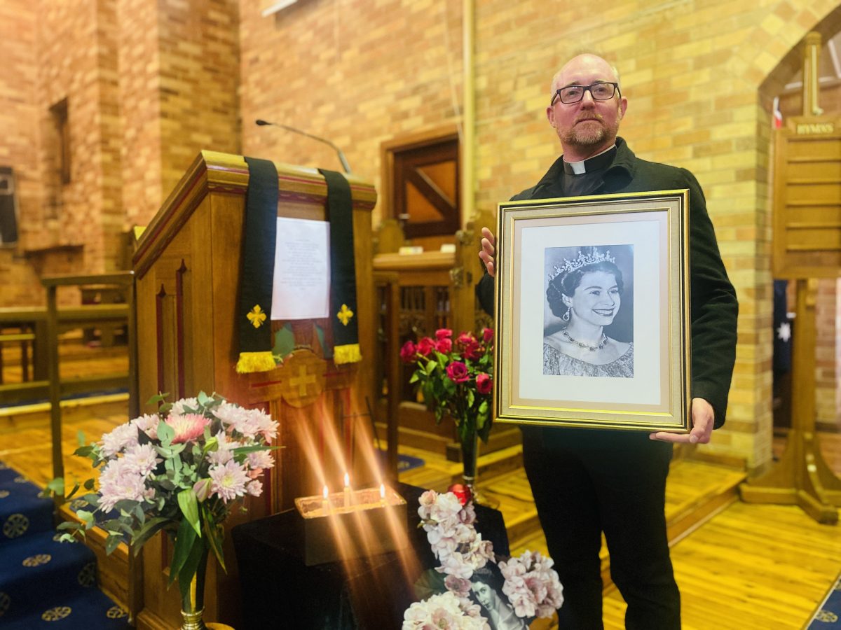 Father Thomas holds Queen's portrait