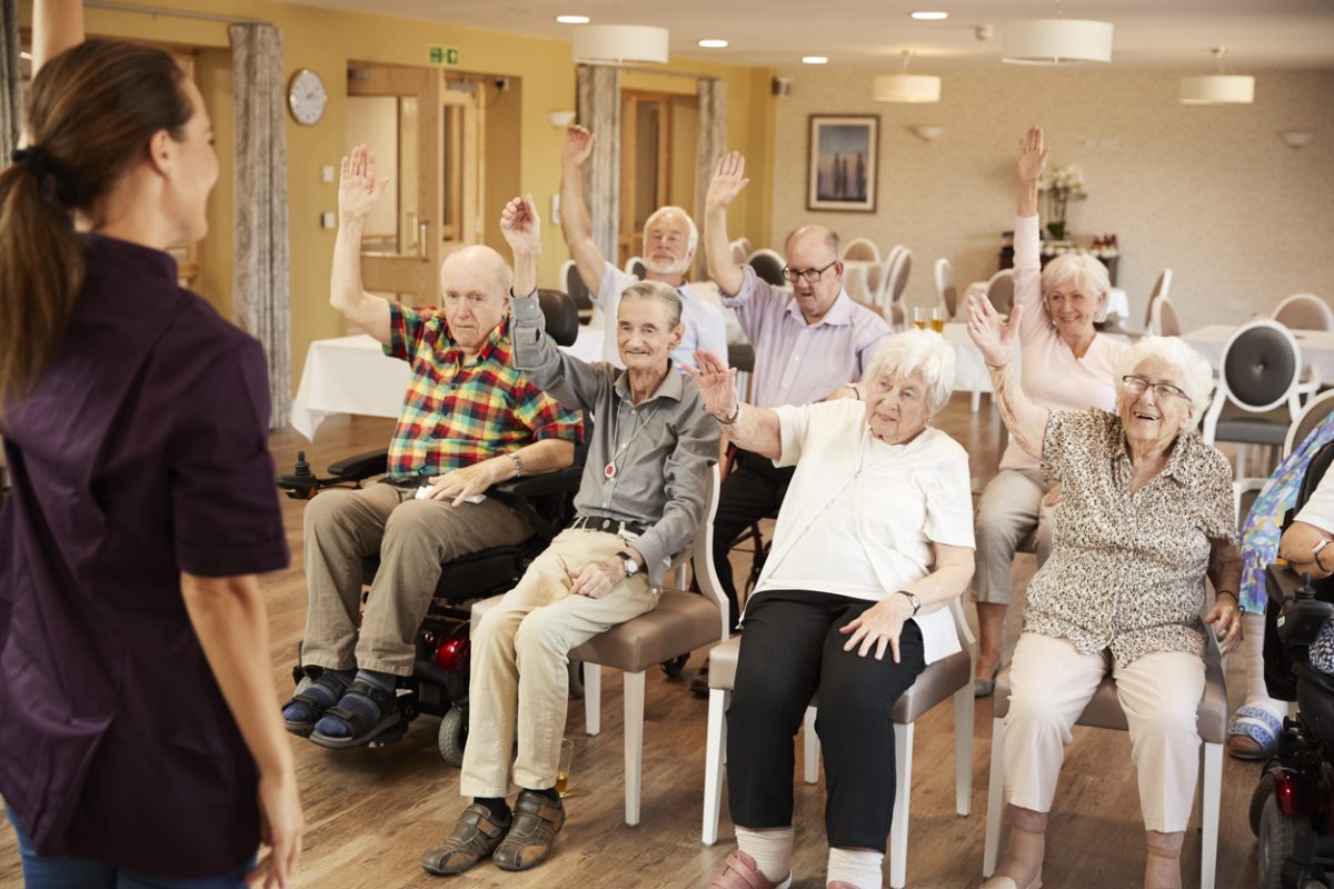 Carer Leading Group Of Seniors In Fitness Class In Retirement Home