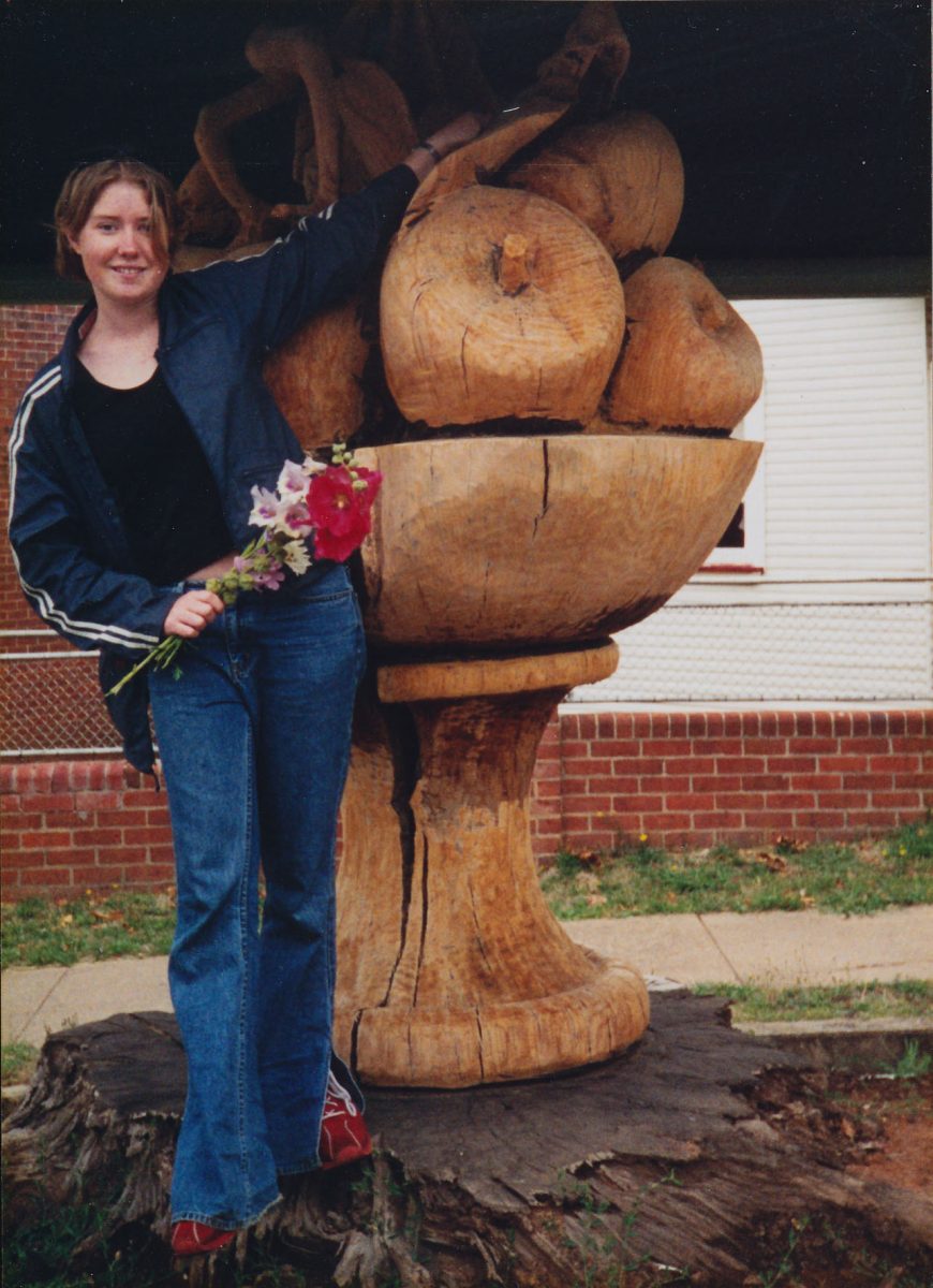 young woman holding flowers while standing next to a sculpture or icon