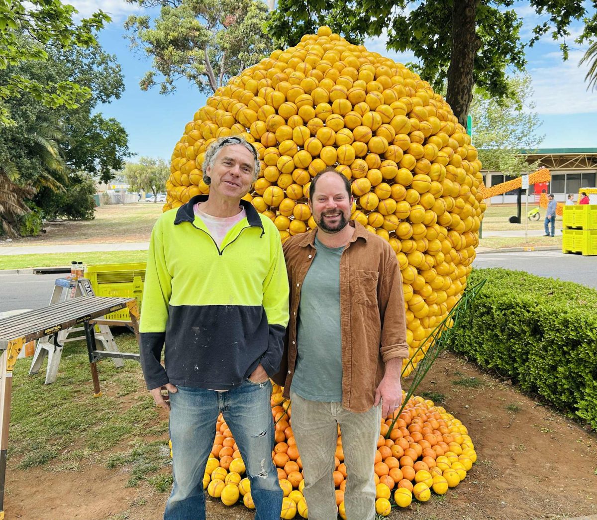 two men in front of a sculpture of a lemon, made mainly from grapefruits 